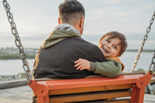 Father and son sitting on swing at park