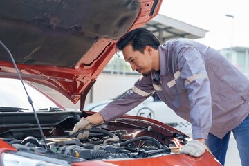 Insurance officer inspecting under car hood. Asian man in uniform, focused on assessment....