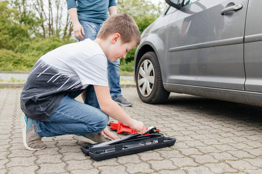 Boy picking up wrench from toolbox by car