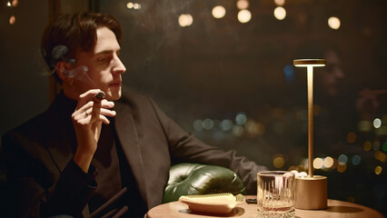 Young man elegantly smokes cigar. Media. Gorgeous man smokes cigar in restaurant. Cinematic cigar...