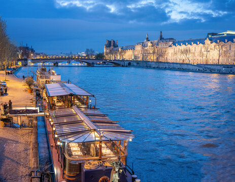 France, Ile-de-France, Paris, Boats moored along Seine at dusk with Louvre Museum in background