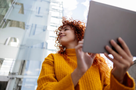 Smiling young woman with curly hair using tablet PC