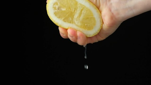 Hand squeezing lemon juice from half a lemon on a black background slow motion.