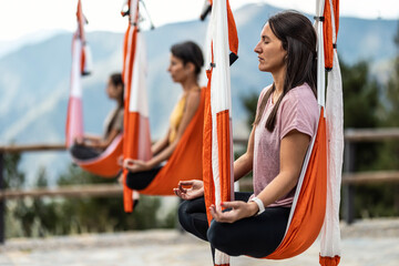 Women with eyes closed meditating on aerial silk practicing yoga in class