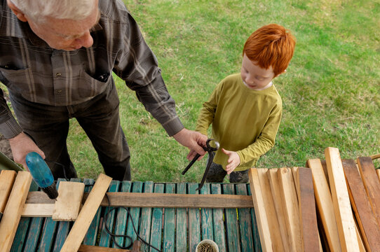 Grandfather giving tool to grandson at back yard