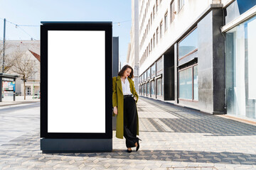 Fashionable businesswoman leaning on blank billboard in city