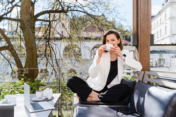 Smiling businesswoman sitting with coffee cup at sidewalk cafe on sunny day