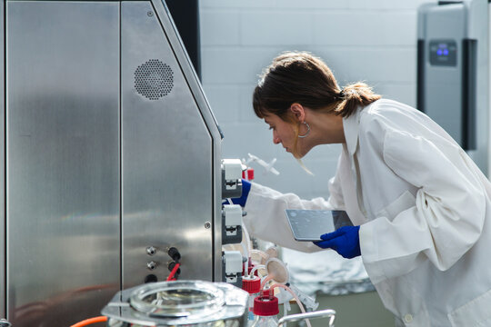Young scientist with tablet PC examining bioreactor in laboratory
