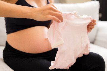 Pregnant woman hold with baby bodysuit at home