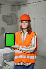Architect woman in vest and hard hat shows tablet with green screen for mockup