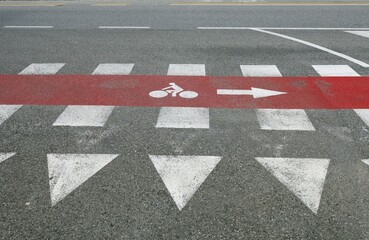 Red bicycle lane sign along a crosswalk, with a painted yield  traffic sign in front. Urban road on...