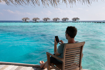 mobile internet abroad in foreign country, online banking, man using smartphone on the beach in Maldives