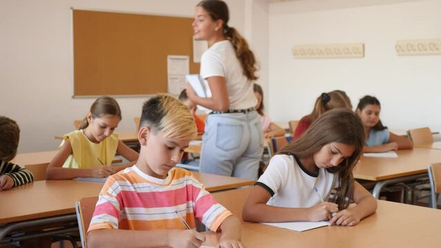 Female teacher reading lecture to schoolkids in classroom. Girl and boys attending teacher's lesson.