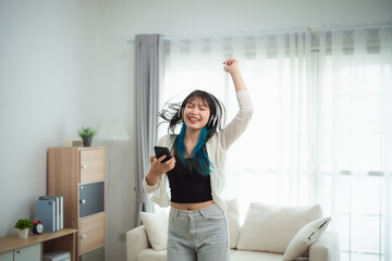 young woman with vibrant blue-tipped hair dances energetically in a modern living room. She wears...