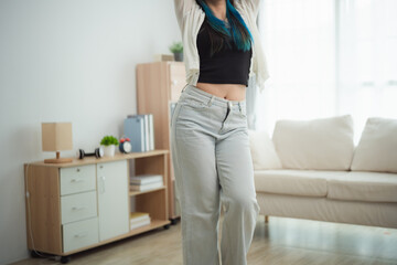 A close-up of a young woman's midsection dances energetically in modern living room. She wears...