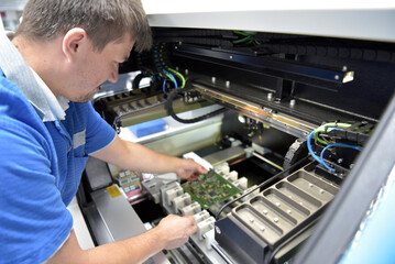 engineer working on a machine for assembly and production of semiconductor boards in an industrial...
