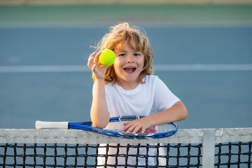 Child playing tennis on outdoor court. Cute little child boy with tennis racket and ball on court.