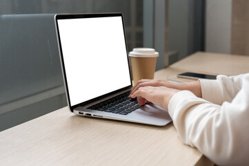 A close-up image of a woman working remotely at a coffee shop, working on her laptop computer.