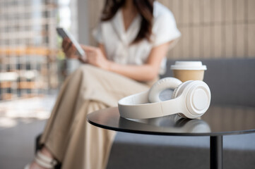 A selective focus image of a takeaway coffee cup and headphones on a coffee table in a coffee shop.