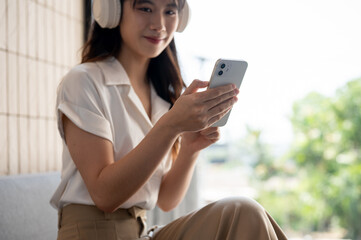A cropped image of a woman is using her smartphone while listening to music on her headphones.