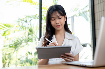 A beautiful Asian businesswoman using a stylus pen on her digital tablet, working in the office.