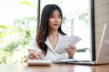 A female accountant is checking bills and receipts, working on business financial data on her laptop