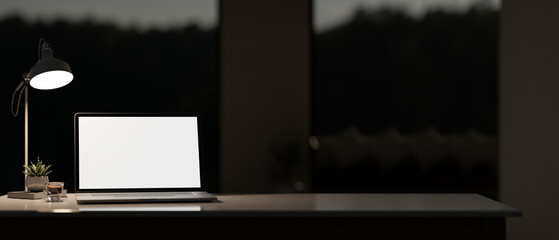 A dark private office or home office at night features a laptop computer mockup on the table.