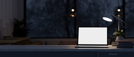 A modern dark office at night features a white-screen laptop computer mockup on the table.
