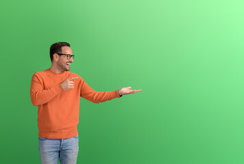 Excited young businessman pointing and advertising new product on empty palm over green background