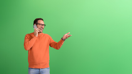 Young cheerful businessman sharing good news over phone call and gesturing against green background