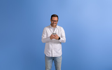 Portrait of smiling male entrepreneur texting online over mobile phone on isolated blue background