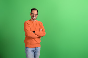 Portrait of young businessman smiling with arms crossed and posing confidently on green background