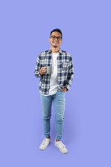 Fototapeta premium Full-length Portrait of a young Asian man smiling while holding a cup standing isolated over a purple background