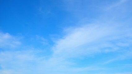 A clear blue sky with a few wispy clouds scattered across it. The bright blue hue of the sky and the soft white clouds create a calm and serene atmosphere. Blue sky background.
