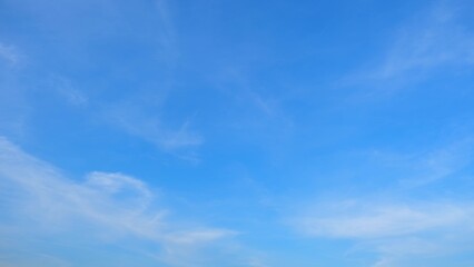 A bright blue sky with a few wispy clouds scattered across. The light blue gradient adds a sense of...