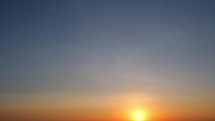A tranquil sunrise with the sun just above the horizon, casting a warm, golden glow. The sky transitions from deep blue at the top to soft orange and yellow near the horizon. Sunrise sky background.

