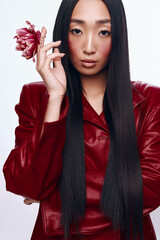 Stylish woman with long black hair and red leather jacket holding a flower