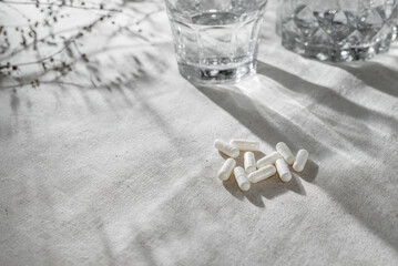 White medication capsules and glass with water on neutral grey table background with sunlight...