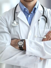Doctor in uniform holding stethoscope and crossed arms. Hospital or clinic background and copy space