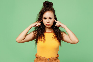 Young sad woman of African American ethnicity wear yellow tank shirt top cover ears with hands...