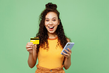 Young surprised woman wear yellow tank shirt top using mobile cell phone hold credit bank card...