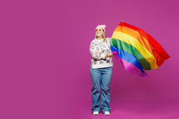 Full body young happy lesbian woman wear pink animal clothes hold in hand rainbow striped flag look aside on area isolated on plain purple background studio. Pride day June month love LGBTQ concept.