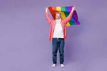 Full body smiling cool happy elderly bearded gay man 50s year old hold striped rainbow flag above...