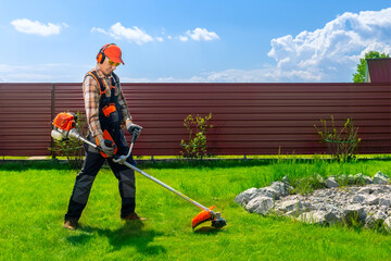Worker, man mowing tall grass with petrol lawn trimmer in the backyard of house.