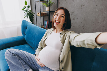 Close up young pregnant woman with belly in casual clothes do mobile cell phone selfie shot sit on...