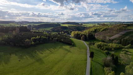 This aerial image features a picturesque landscape of rolling hills covered in lush greenery,...