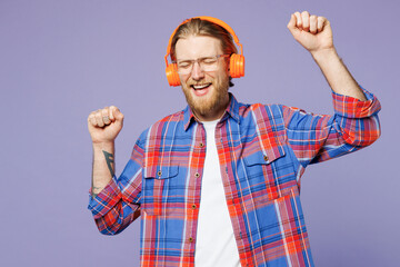 Naklejka premium Young smiling fun happy man he wears blue shirt casual clothes listen to music in headphones raise up hands dance isolated on plain pastel light purple background studio portrait. Lifestyle concept.