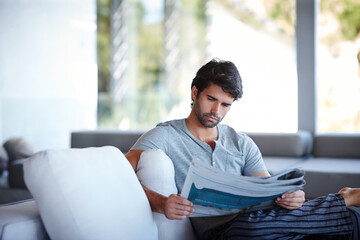 Home, man and newspaper for reading on sofa in living room for information, story or news. House,...