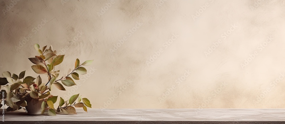 Poster beige textured wall behind an empty table with glossy leaves on the wall creating a composition with