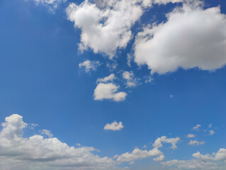 A bright, clear blue sky with scattered fluffy cumulus clouds, suggesting a calm and sunny day.
